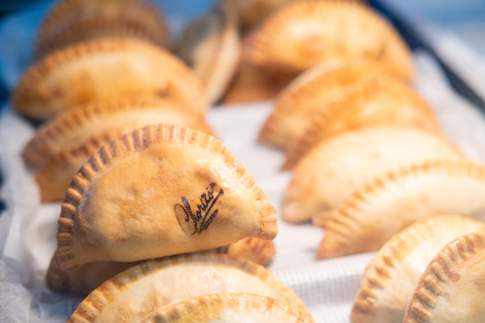 Fried pastries shaped like half-moons, some with a signature or marking on one, arranged on white paper.